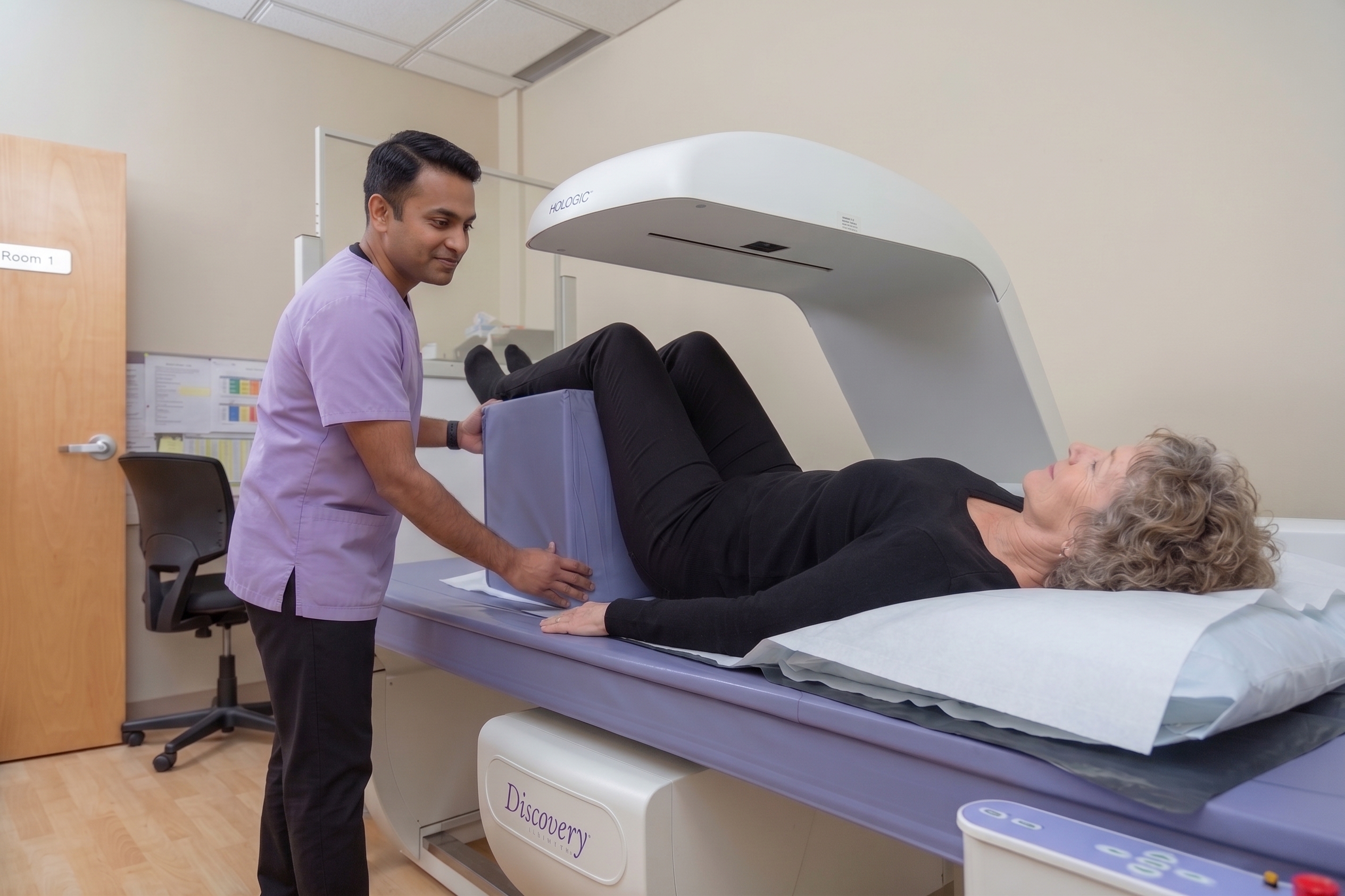A male clinician guiding a patient lying on a bone mineral density (BMD) scanner bed.